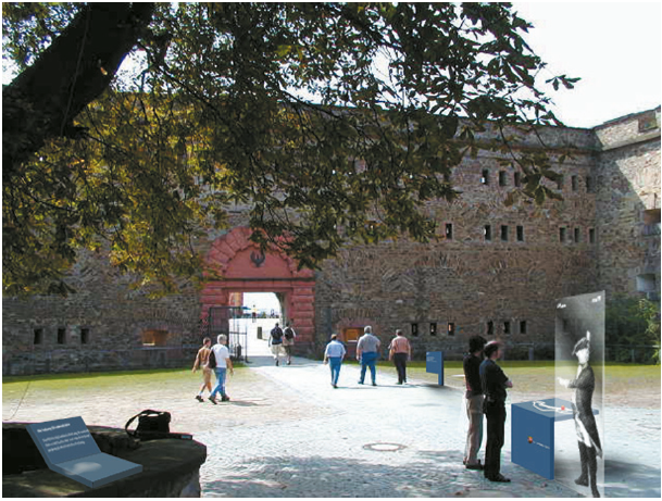 Durchgang zum Hauptplatz der Festung mit verschiedenen Infoelementen, darunter Lageplan mit Standort, Hinweisschild und historischen Hintergrundinformationen.